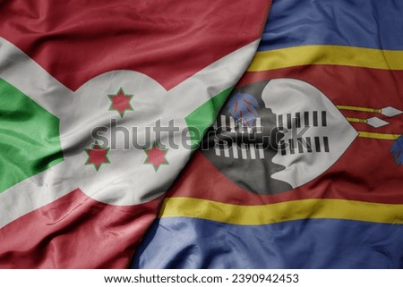 big waving national colorful flag of eswatini and national flag of burundi . macro