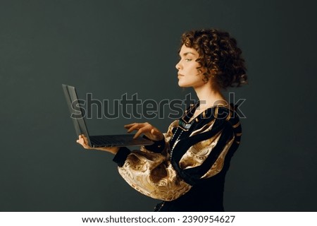 Young adult woman dressed in a medieval dress working on a laptop. Profile portrait