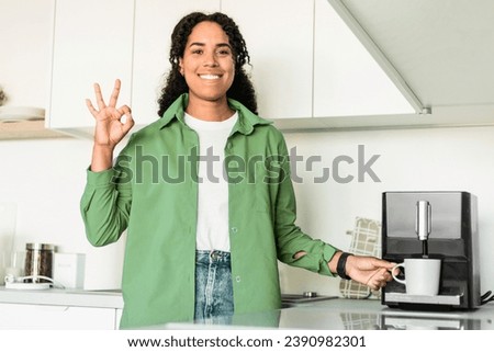 Smiling Black Young Lady Making Coffee Via Machine And Gesturing Okay To Camera In Modern Home Kitchen Interior. Woman Approving Coffee Maker With Ok Sign In The Morning