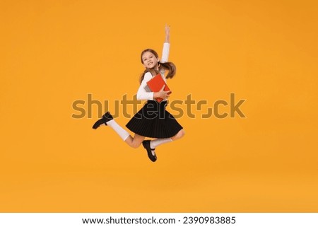 Happy schoolgirl with books jumping on orange background Royalty-Free Stock Photo #2390983885