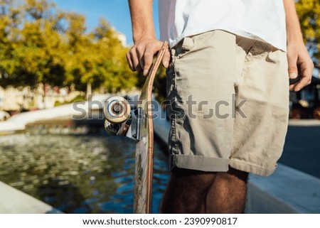 Crop man holding skateboard near water