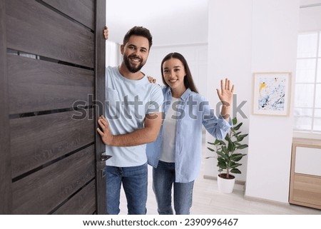 Happy couple waving near door. Invitation to come indoors Royalty-Free Stock Photo #2390996467