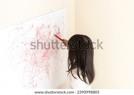 A girl (3 years old, Japanese) scribbling on a whiteboard on the wall