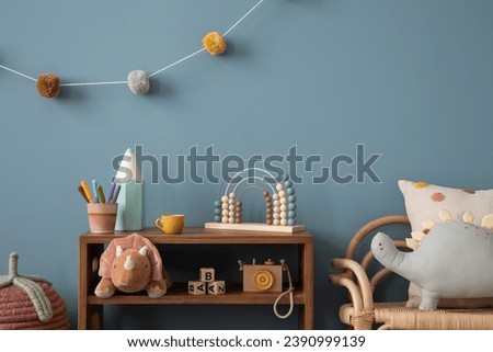 Aesthetic composition of warm child room interior with wooden sideboard, blue wall, stylish armchair, garland on wall, plush monkey, toys, wooden camera and personal accessories. Home decor. Template.