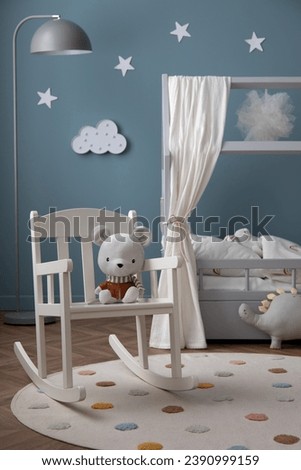 Creative composition of cozy kid room interior with stylish bed, round rug, white chair, plush bear, stars ornament, gray lamp, ornament on wall and personal accessories. Home decor. Template. 