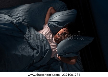 Annoyed man suffering neighbour noise in the bedroom at night at home. He can't sleep at night. Noise and insomnia concept. Copy space Royalty-Free Stock Photo #2391001931