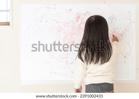 Back view of a girl scribbling on a whiteboard on the wall (3 years old, Japanese)