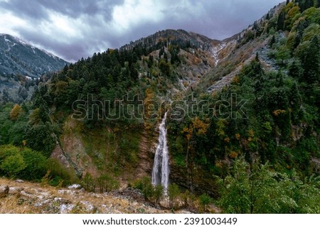 Photo of a waterfall in autumn. The water coming out of the stones flows in the form of a waterfall. Waterfall view with clouds.