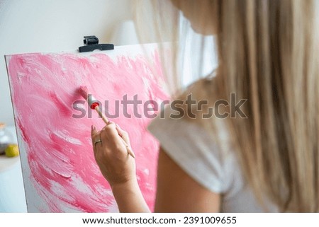 Close up view of young woman artist with palette and brush painting abstract pink picture on canvas at home. Back view. Art and creativity concept. High quality photo