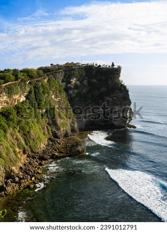 Uluwatu temple on Bali, Indonesia. Beautiful Indian Ocean around. Deep blue expanse meets rugged cliffs. The waves gently caress the rocky shoreline, creating a harmonious dance between water and land