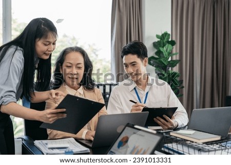 Business documents on office table with tablet and laptop computer and chart and team colleagues discussing data in office.