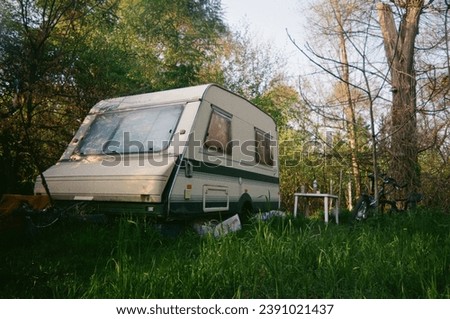 An abandoned trailer in the middle of a green forest. The photo was taken on film.