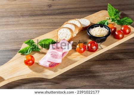 A polished board with cherry tomatoes, mint, ham, baguette, and Parmesan—a refined complement to spaghetti bolognese. The bamboo-like wood texture enhances the stylish food arrangement