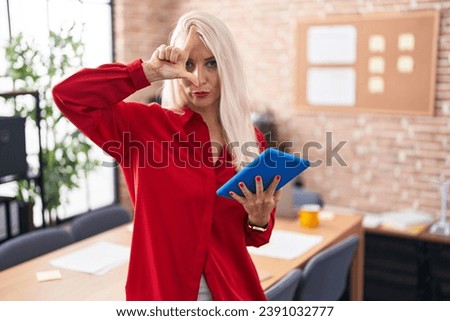 Caucasian woman working at the office with tablet making fun of people with fingers on forehead doing loser gesture mocking and insulting. 