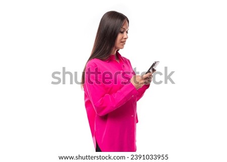 young brunette lady dressed in a bright pink shirt is chatting in a smartphone in a social network