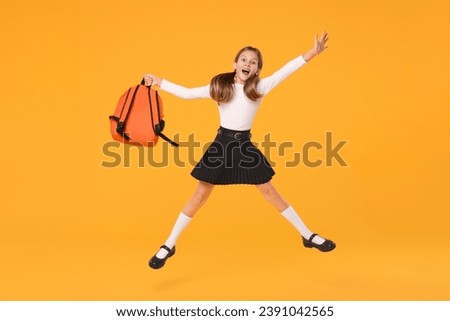 Happy schoolgirl with backpack jumping on orange background Royalty-Free Stock Photo #2391042565