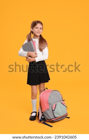 Happy schoolgirl with backpack and books on orange background Royalty-Free Stock Photo #2391042605