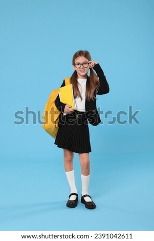 Happy schoolgirl with backpack and books on light blue background Royalty-Free Stock Photo #2391042611