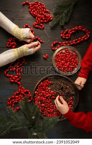 Children make garlands with their own hands. Red rosehip garlands using natural materials to decorate the Christmas tree.