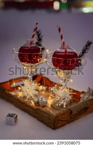 Two Christmas cocktails in the shape of Christmas tree toys on a wooden serving platter and snow-covered table. The composition is illuminated by a garland.  Holiday concept. 