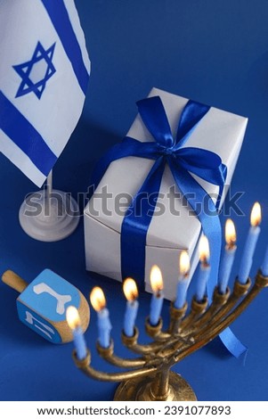 Menorah, dreidel, and gift for Hanukkah celebration on color background, closeup