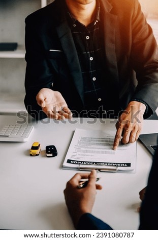 A car rental company employee is handing out the car keys to the renter after discussing the rental details and conditions together with the renter signing a car rental agreement. Concept car rental. Royalty-Free Stock Photo #2391080787