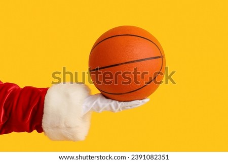 Santa Claus holding ball for playing basketball on yellow background, closeup