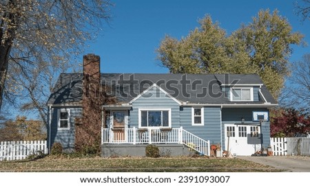 Blue, one-story house with outside clutter has white trim, railing and fence in autumn season. 