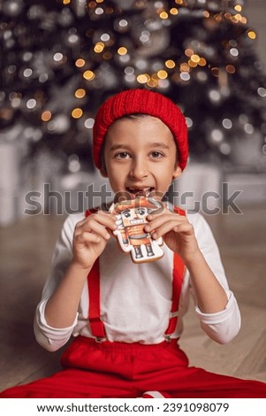 Merry Christmas kid. Portrait of a happy funny cute baby boy child one 6 years old in red clothes holding a Christmas gingerbread with a picture on it. New Year's Eve . Vertical