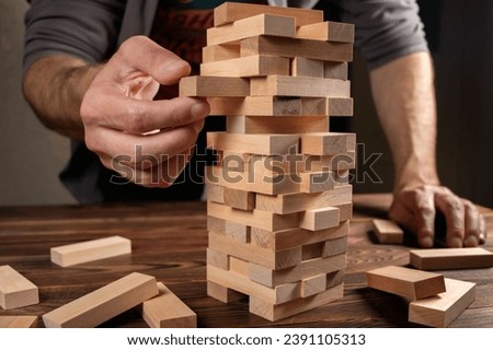 Hand of engineer playing a blocks wood tower game jenga on blueprint or architectural project. Royalty-Free Stock Photo #2391105313