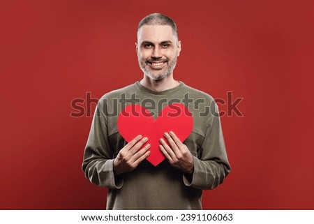 man smiling, holding a paper heart with both hands