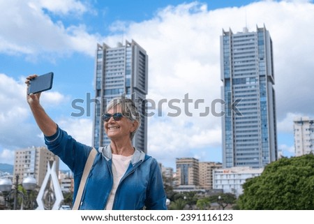 Senior smiling woman with short hair visiting and traveling in Santa Cruz de Tenerife using the phone to take pictures of city