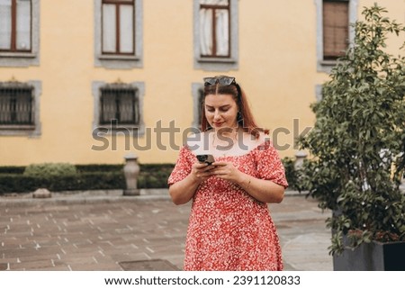 Picture of pretty young woman staying on the street holding phone in hands. 30s tourist in dress walking on old city street checks her smartphone. Use technology concept, Traveling Europe in summer
