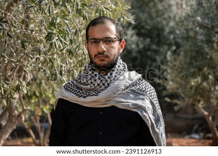 portrait for male wearing keffiyeh in olive tree field with black background and black shirts also with angry facial expression Royalty-Free Stock Photo #2391126913