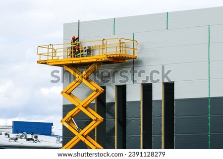 Large elevated aerial scissor lift working platform with workers against grey sandwich panels wall Royalty-Free Stock Photo #2391128279