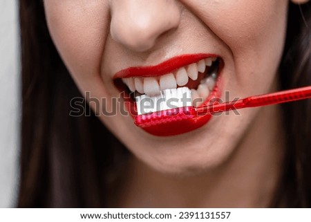 A woman brushing her teeth with a red toothbrush. A Morning Routine: Woman Energizing Her Teeth with a Vibrant Red Toothbrush Royalty-Free Stock Photo #2391131557