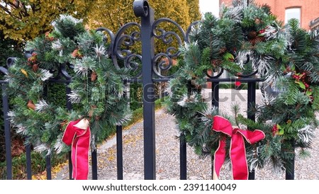 Two evergreen wreaths tied with red ribbon on a gate.  Royalty-Free Stock Photo #2391140049