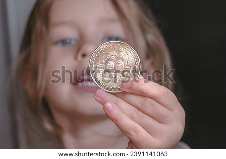 Little girl holding a coin with bitcoin symbol in her hand.