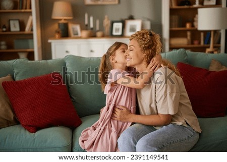 Cute little girl kissing her mother on sofa in living room