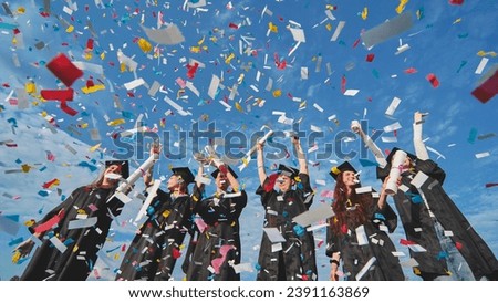 Happy graduates throw colorful confetti against a blue sky. Royalty-Free Stock Photo #2391163869