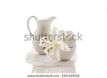 white dishes, jug and bowls with a white lily flower on an openwork napkin on a white background