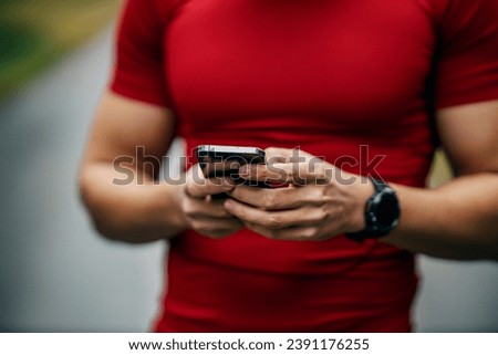 Cropped picture of sportsman's hands using cellphone outdoors.