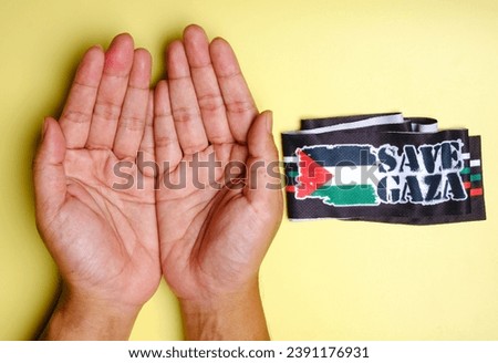 A picture of Muslim praying hand with Palestinian flag and Save Gaza word. Pray for Gaza concept.