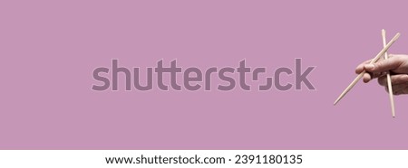 Asian chopsticks held in human hand on monochrome pink background. Without food. No identifiable person. Wide free space for layout of text and other content