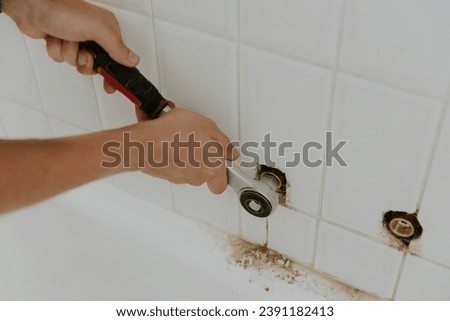 A young man tightens the nut of the faucet in the bathroom with a ratchet. Royalty-Free Stock Photo #2391182413