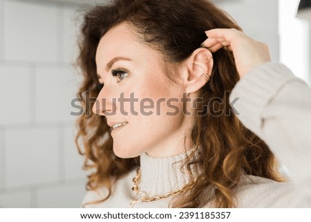 Cropped close-up shot of a young woman with two asymmetrical golden ear cuffs. Female with golden ear cuffs, side view. Royalty-Free Stock Photo #2391185357