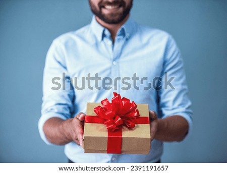 Cropped image of handsome bearded man in smart casual wear holding a gift box and smiling, on gray background