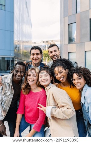 Vertical portrait of young group of diverse people smiling at camera outdoors. Happy millennial college students enjoying time together, social gathering and hanging out at city street.