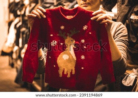 Warm red knitted Christmas sweater with a picture of a cute deer in woman's hands. Choosing clothes for a kid, child. Young mother buying clothes for a New Year present. Winter sales. Vintage store.