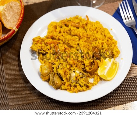Appetizing racy seafood paella with mussels, calamari rings and prawns served with lemon. Authentic Valencian cuisine.. Royalty-Free Stock Photo #2391204321